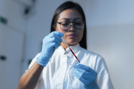 Female lab researcher placing a sample on a microscope flat glass slide, dripping blood drops with a pipette. Laboratory expertise concept.の写真素材
