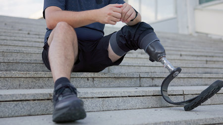 A person rests on outdoor steps, showcasing a prosthetic leg while taking a break. The atmosphere is calm and relaxed.の写真素材