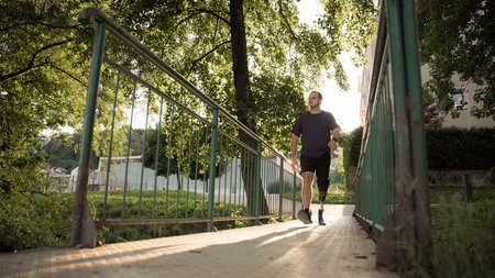A man is walking on a path surrounded by trees during a sunny evening. The scene is serene and...