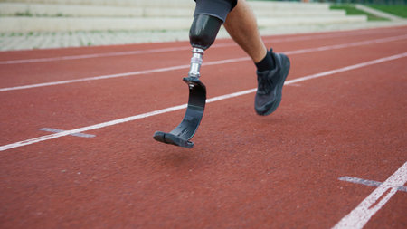Athlete with a prosthetic leg runs on a track during a bright day, showcasing determination and strength.の写真素材