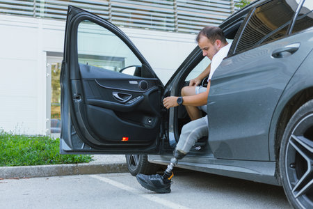 A person with a prosthetic leg is stepping into a car parked in a lot on a sunny day.の写真素材