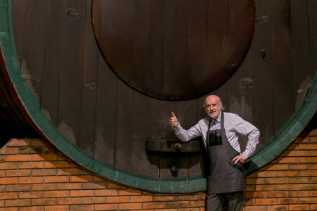 A craftsman gives a thumbs up by an old wine barrel in a cozy cellar, highlighting winemaking...