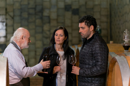 Three people engage in a wine tasting experience at a vineyard, discussing flavors and aromas while enjoying red wine.の写真素材