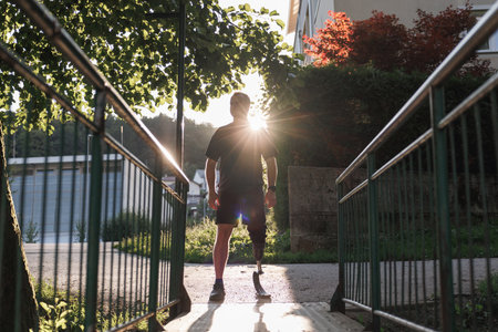Recreational athlete with disability, walking across the small steel bridge at the greenway using a...
