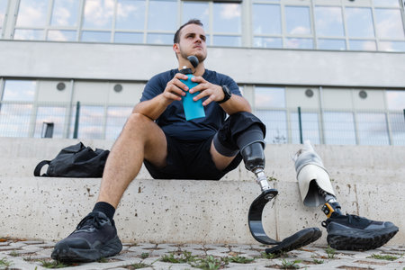 Athlete with leg amputation resting on outdoor steps after workout. Strength, motivation, and...