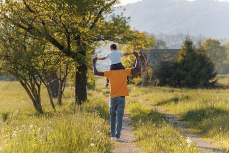 Joyful African American little boy enjoying a walk on his father shoulders under warm sunlight in nature. Childhood, happiness, and freedom concept.の写真素材