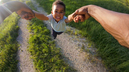 Point of view POV of a dad twirling his little son in a circle, holding his hands, enjoying cheerful family fun, outdoor play, and a carefree childhood.の写真素材