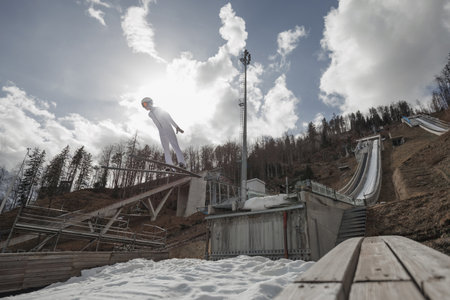 A ski jumper takes flight against a backdrop of clouds and trees, showcasing skill and bravery in the sport.の写真素材