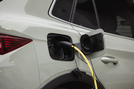 A car is being charged at an electric station with a yellow charging cable connected to its port.