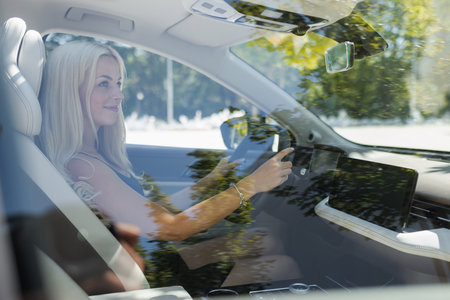 A woman is driving a car with trees and sunlight visible outside the window. She appears focused on the road ahead.の写真素材