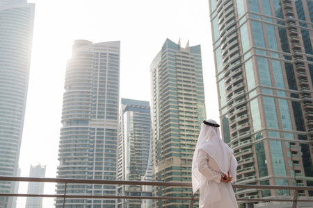 Emirati businessman wearing traditional white clothing looking at real estate investments and...