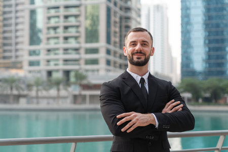 Confident businessman stands with arms crossed in modern Dubai, showing leadership and professional success in a busy urban setting.の写真素材