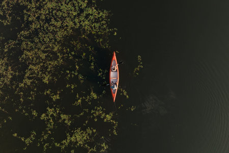 Man and woman paddle together on a lake while surrounded by green plants and mountain views during a...