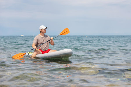 Young man enjoys paddleboarding on the sea under the sun during a summer day. He is active and engages in outdoor fun by the beach.の写真素材