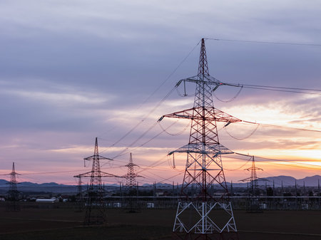 Power lines and electrical towers stand in a rural area as the sun sets, showcasing energy...