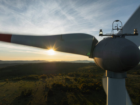 Wind turbines stand tall on hills as the sun sets, showcasing renewable energy and clean power...