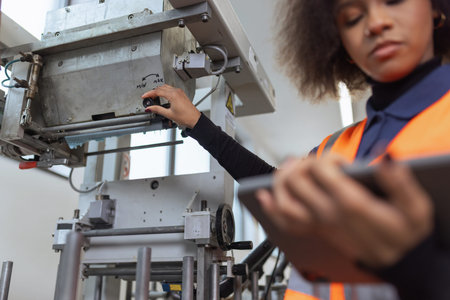 African American woman, worker in the metal industry using a tablet for equipment diagnostics and...