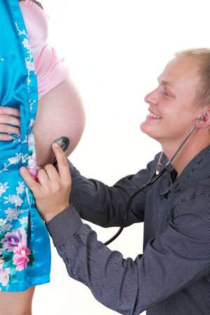 young pregnant woman with man listening her with phonendoscope isolated on white の写真素材