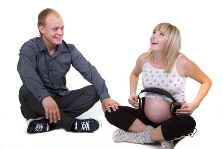 young pregnant woman with man listening with headphones isolated on white の写真素材
