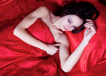 Beautiful brunette girl sleeping on red silkの写真素材