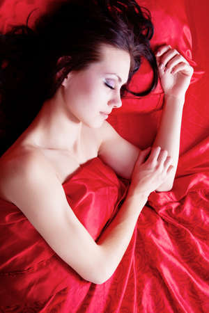 Beautiful brunette girl sleeping on red silkの写真素材