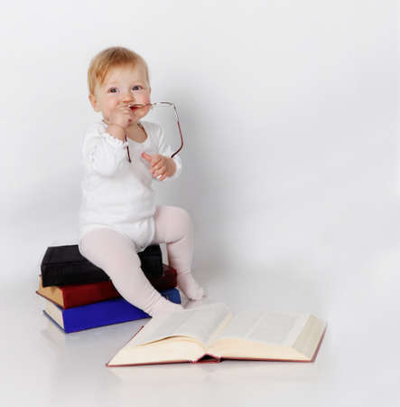 Little girl sitting on the books with glasses in handsの写真素材