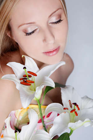 Beautiful blond girl with lily flower near faceの写真素材