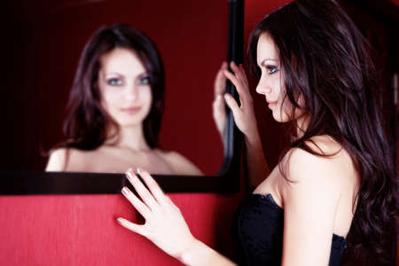 Beautiful brunette girl looking to the mirror in red roomの写真素材