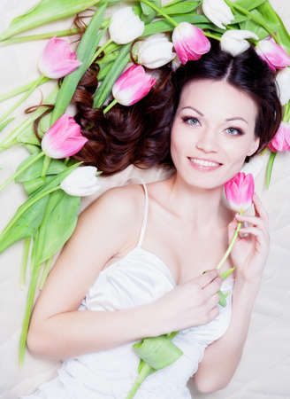 Beauriful brunette girl laying in bed with tulip flowersの写真素材