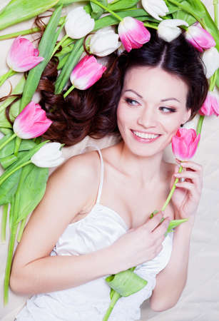 Beauriful brunette girl laying in bed with tulip flowersの写真素材