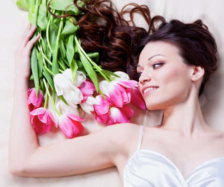 Beauriful brunette girl laying in bed with tulip flowersの写真素材
