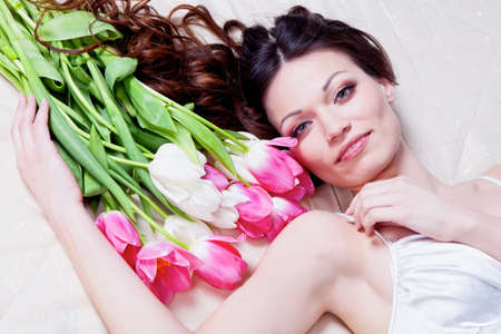 Beauriful brunette girl laying in bed with tulip flowersの写真素材