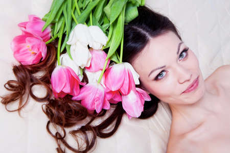 Beauriful brunette girl laying in bed with tulip flowersの写真素材