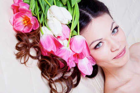 Beautiful brunette girl laying in bed with tulip flowersの写真素材