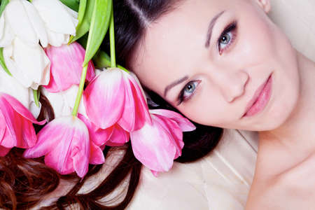 Beautiful brunette girl laying in bed with tulip flowersの写真素材