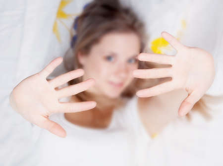 Young beautiful girl lying in bed and show her handsの写真素材