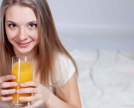 Young beautiful girl drinking fruit juice in bedroomの写真素材