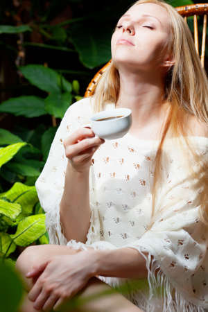 Beautiful girl with cup in hands sitting in gardenの写真素材