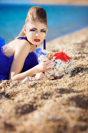 Beautiful girl lying on the beach with seashell in handsの写真素材