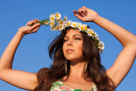 Girl in camomile wreath with blue sky at backgroundの写真素材