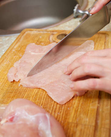 Hand with knife cutting chicken meatの写真素材