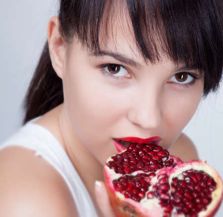 Brunette girl with garnet fruit in studioの写真素材