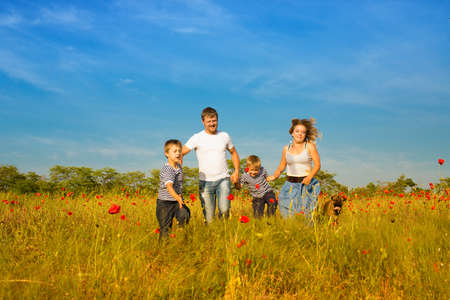 Family of four person and dog playing on the poppy fieldの写真素材