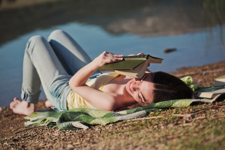 Beautiful woman reading book near the mountain lakeの写真素材