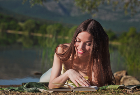 Beautiful woman reading book near the mountain lakeの写真素材