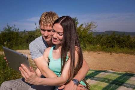 Young couple using tablet pc near the mountain lakeの写真素材