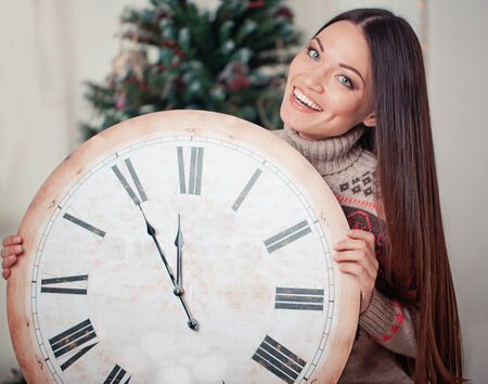 Beautiful young woman with big clock on 11:55PM near christmas treeの写真素材