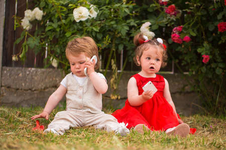 Little boy and girl playing with cellphones in the gardenの写真素材