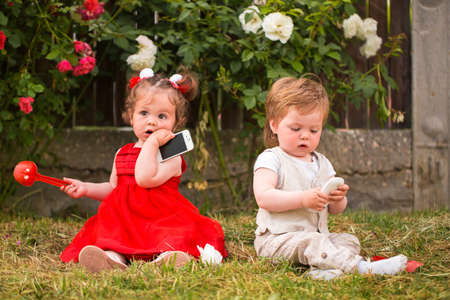 Little boy and girl playing with cellphones in the gardenの写真素材