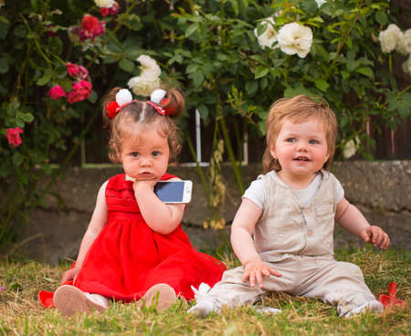 Little boy and girl playing with cellphones in the gardenの写真素材